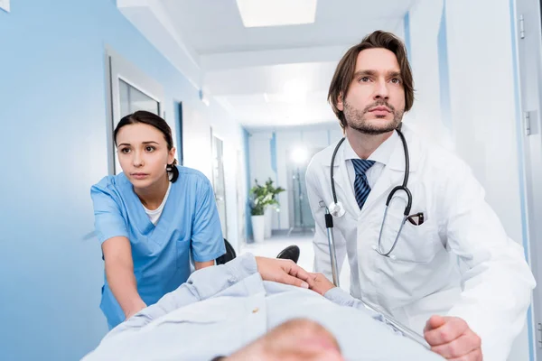 Serious doctors with stethoscope transporting patient on gurney — Stock Photo