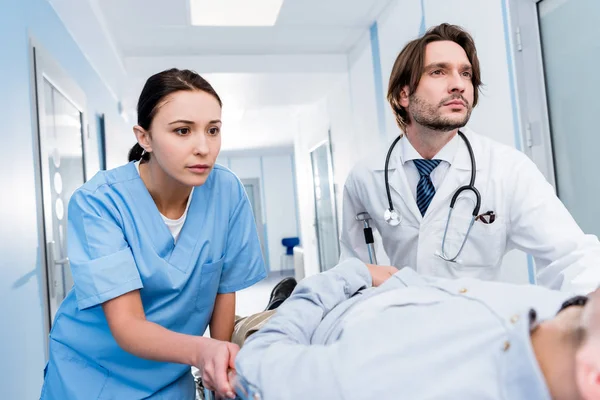 Serious doctors in uniform transporting patient on gurney — Stock Photo