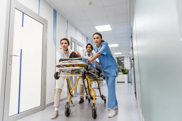 Worried doctors and nurse transporting unconscious patient on gurney — Stock Photo