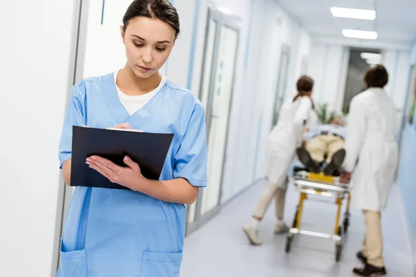 Geballte Krankenschwester in blauer Uniform schreibt Notizen in Klemmbrett — Stockfoto