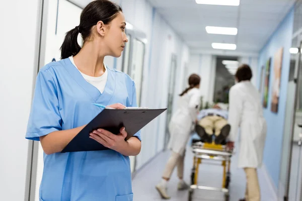 Брюнетка медсестра у синій формі писати замітки в буфер обміну — стокове фото