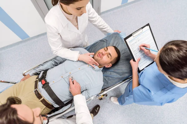 Top view of doctors transporting unconscious patient and checking pulse — Stock Photo