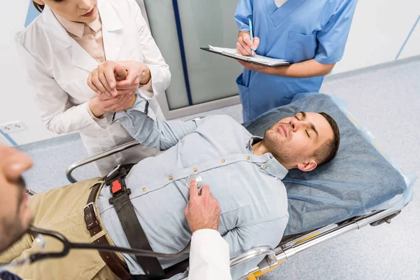 Vista cortada de médicos e paciente doente deitado na maca na clínica — Fotografia de Stock
