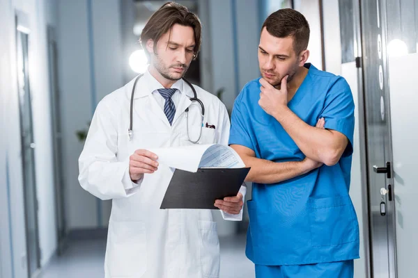Pensive doctor holding clipboard and discussing diagnosis with nurse — Stock Photo