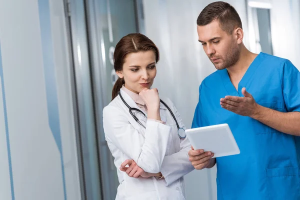 Médecins pensifs avec tablette numérique debout dans le hall — Photo de stock