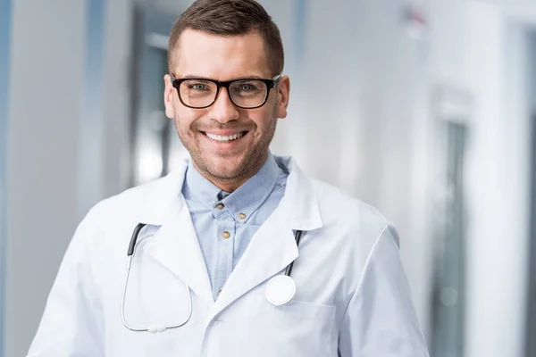 Médico sonriente con estetoscopio mirando la cámara - foto de stock
