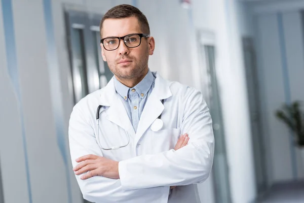 Молодой доктор в очках стоит со скрещенными руками — стоковое фото