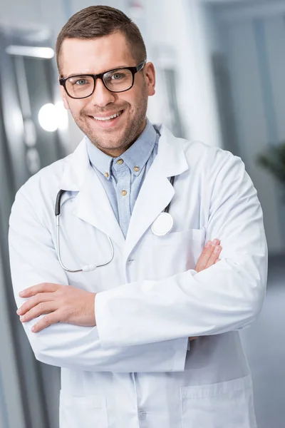 Heureux médecin dans des lunettes debout avec les bras croisés — Photo de stock