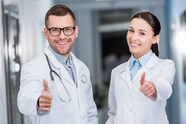 Laughing doctors in white coats showing thumbs up — Stock Photo