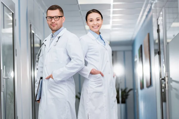 Confident doctors in white coats standing with hands in pockets — Stock Photo