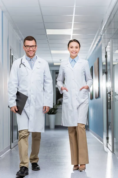 Happy doctors in white coats walking down hall together — Stock Photo