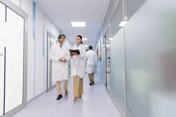 Médecins en manteaux blancs avec dossier noir marchant dans le hall — Photo de stock