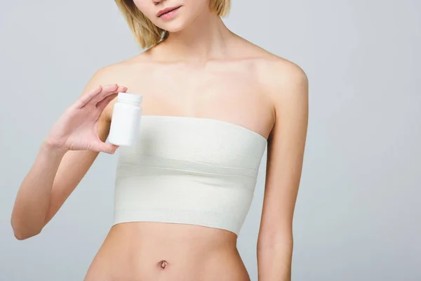 Обрізаний вид жінки в бинті на грудях після пластичної хірургії, що тримає пляшку таблеток, ізольовані на сірому — стокове фото