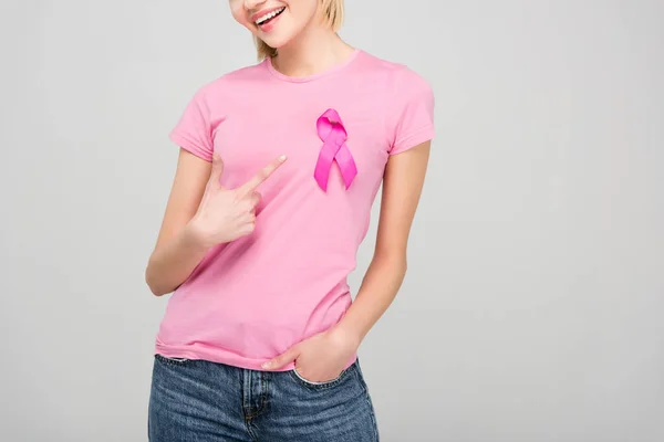 Vista recortada de una mujer joven apuntando a una camiseta rosa con cinta de concienciación sobre el cáncer de mama, aislada en gris - foto de stock