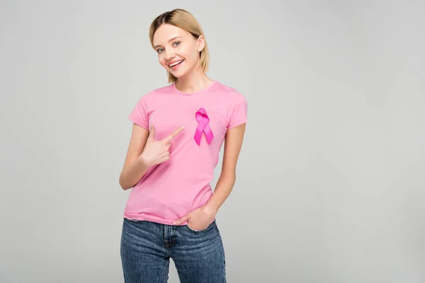 Felice ragazza che punta a t-shirt rosa con nastro di consapevolezza del cancro al seno, isolato su grigio — Foto stock