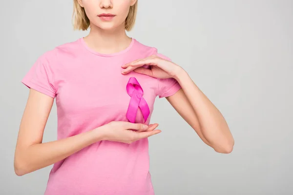 Vista recortada de una mujer joven posando en camiseta rosa con cinta de concienciación sobre el cáncer de mama, aislada en gris - foto de stock