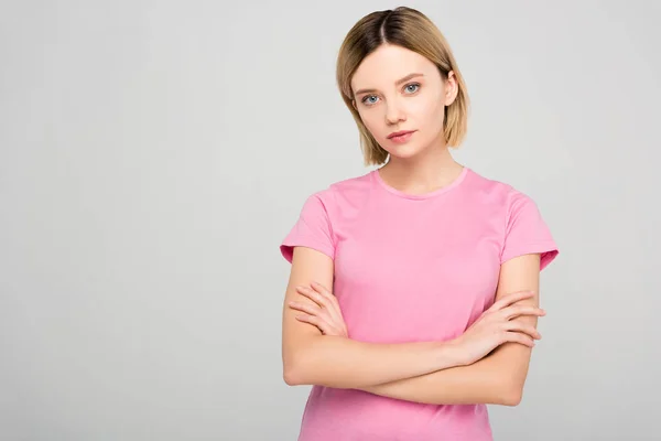 Beautiful blonde woman in pink t-shirt posing with crossed arms, isolated on grey — Stock Photo