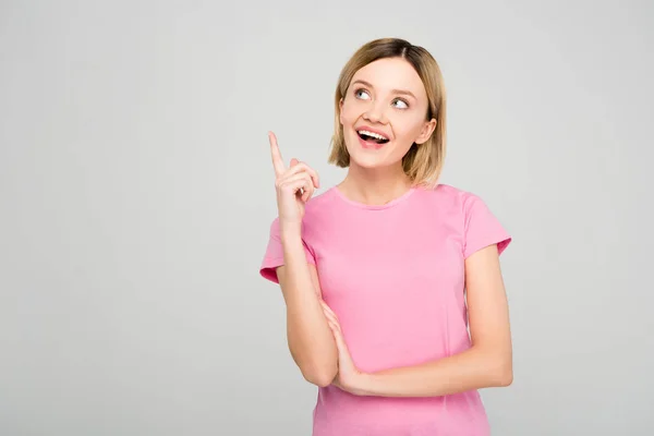 Eccitata giovane donna in t-shirt rosa avere idea, mentre punta su isolato sul grigio — Foto stock