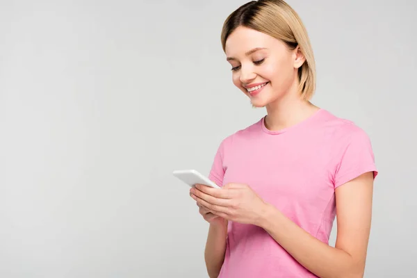 Chica rubia sonriente en camiseta rosa con teléfono inteligente, aislado en gris - foto de stock