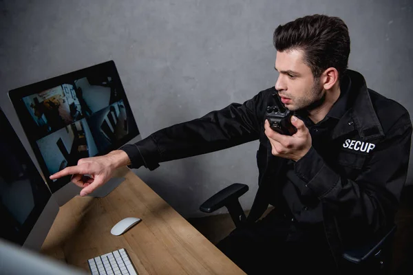 Guardia in uniforme che parla sul walkie-talkie e guarda il monitor del computer — Foto stock