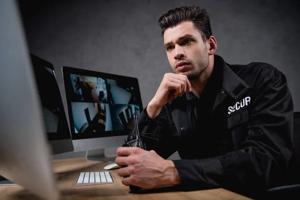 Focused guard in uniform looking at computer monitor and holding walkie-talkie — Stock Photo