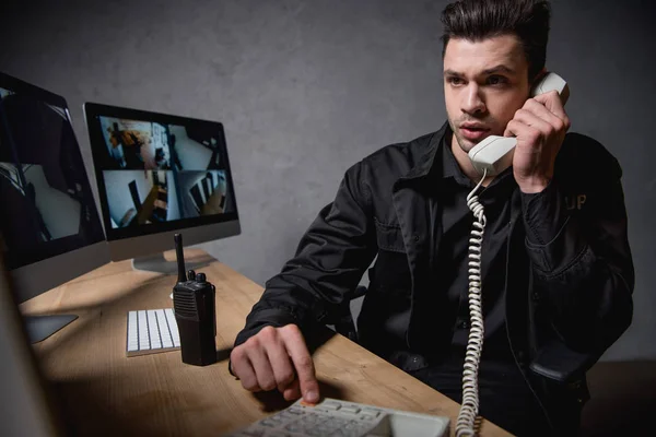 Wachmann in Uniform telefoniert und blickt auf Computermonitor — Stockfoto