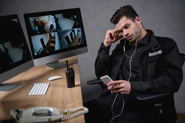 Müder Wachmann in Uniform hört Musik und nutzt Smartphone — Stockfoto