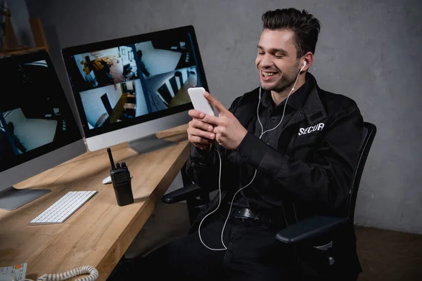 Smiling guard in uniform listening music and using smartphone — Stock Photo