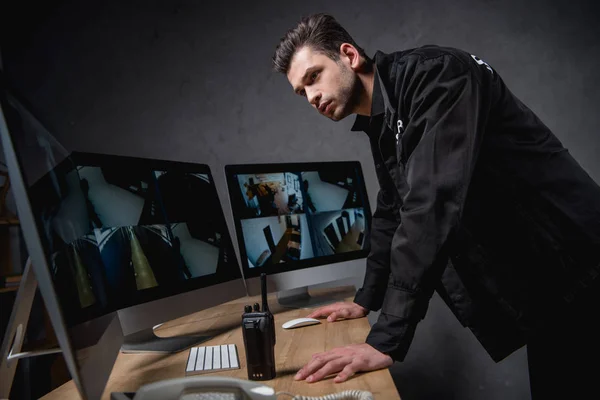 Сфокусированный охранник в форме, смотрящий на монитор компьютера на рабочем месте — стоковое фото