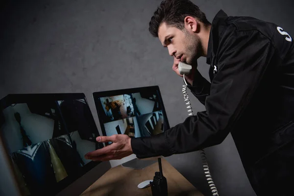 Guardia hablando por teléfono y mirando el monitor de la computadora - foto de stock