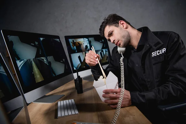 Guardia en uniforme comiendo comida chatarra y hablando por teléfono - foto de stock