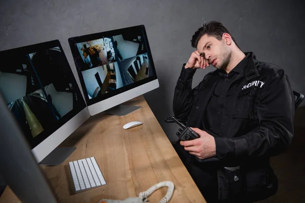 Bored guard in uniform holding walkie-talkie and looking at computer monitor — Stock Photo