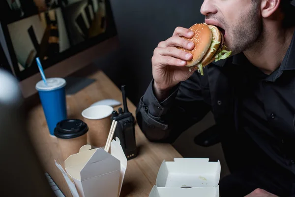Vista recortada de guardia comiendo hamburguesa en el lugar de trabajo - foto de stock