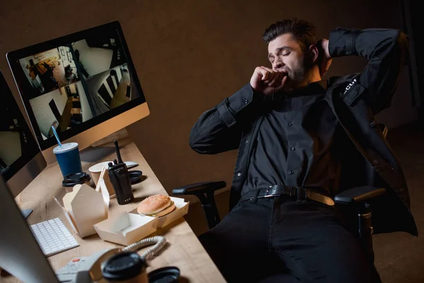 Wachmann in schwarzer Uniform mit verschränkten Armen gähnt am Arbeitsplatz — Stockfoto