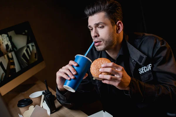 Guardia bebiendo y sosteniendo hamburguesa en el lugar de trabajo - foto de stock