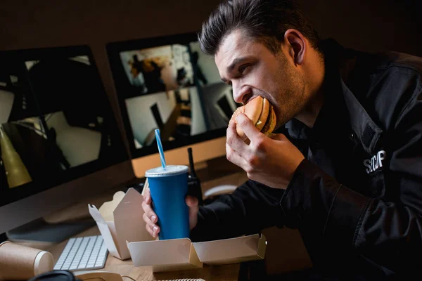 Guarda comer hambúrguer e segurar copo de papel no local de trabalho — Fotografia de Stock