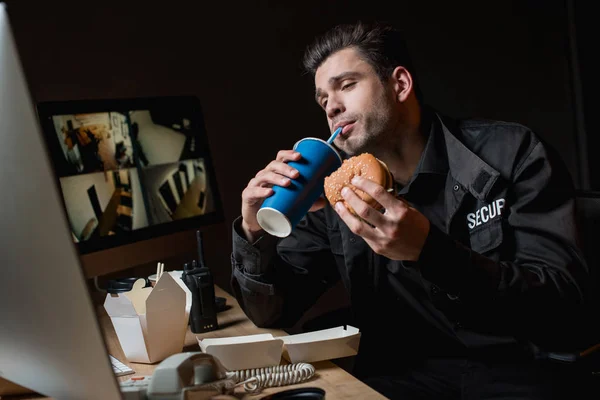 Handsome guard drinking and eating burger at workplace — Stock Photo