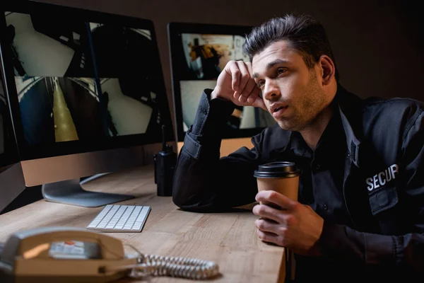 Gelangweilte Wache hält Pappbecher in der Hand und blickt auf Computermonitor — Stockfoto