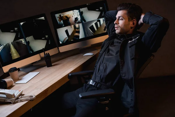 Guardia en uniforme con brazos cruzados mirando el monitor de la computadora - foto de stock