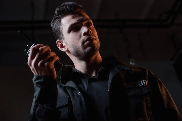 Handsome guard in uniform holding walkie-talkie and looking away — Stock Photo