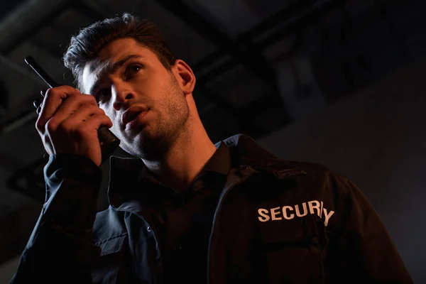 Handsome guard in uniform using walkie-talkie and looking away — Stock Photo