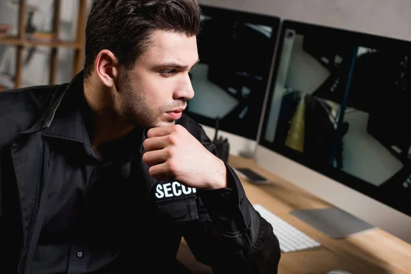 Gardien réfléchi en uniforme regardant le moniteur d'ordinateur sur le lieu de travail — Photo de stock