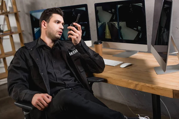 Handsome guard in uniform talking on walkie-talkie at workspace — Stock Photo