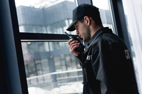 Guapo guardia en uniforme negro hablando en walkie-talkie - foto de stock