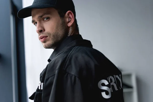 Guapo protector en uniforme negro con auriculares mirando a la cámara - foto de stock