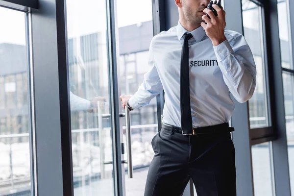 Recortado vista de guapo guardia en traje hablando en walkie-talkie - foto de stock