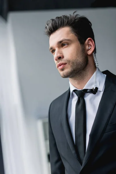 Thoughtful bodyguard in suit with earphone looking away — Stock Photo