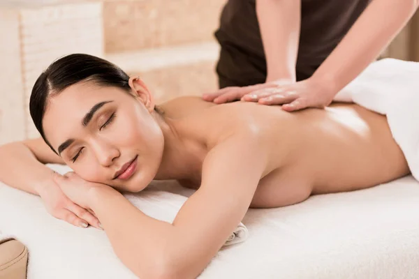 Обрезанный вид массажера, делающего массаж спины красивой азиатской женщине — стоковое фото