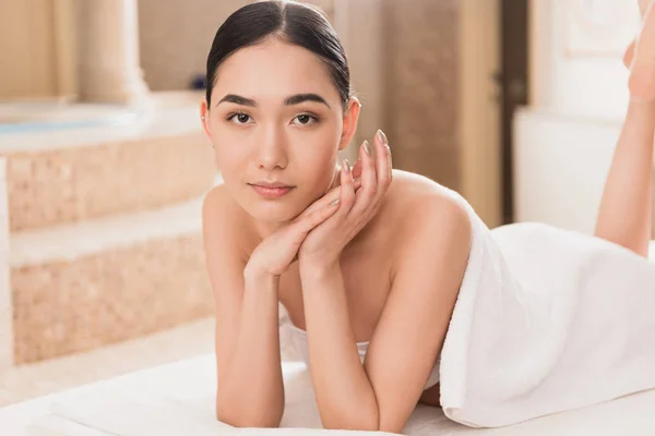 Beautiful asian woman in towel lying and looking at camera — Stock Photo