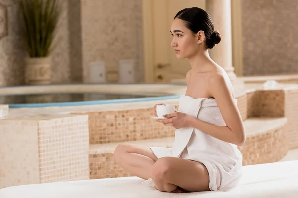 Hermosa mujer asiática en toalla sentado con taza de café en el spa - foto de stock